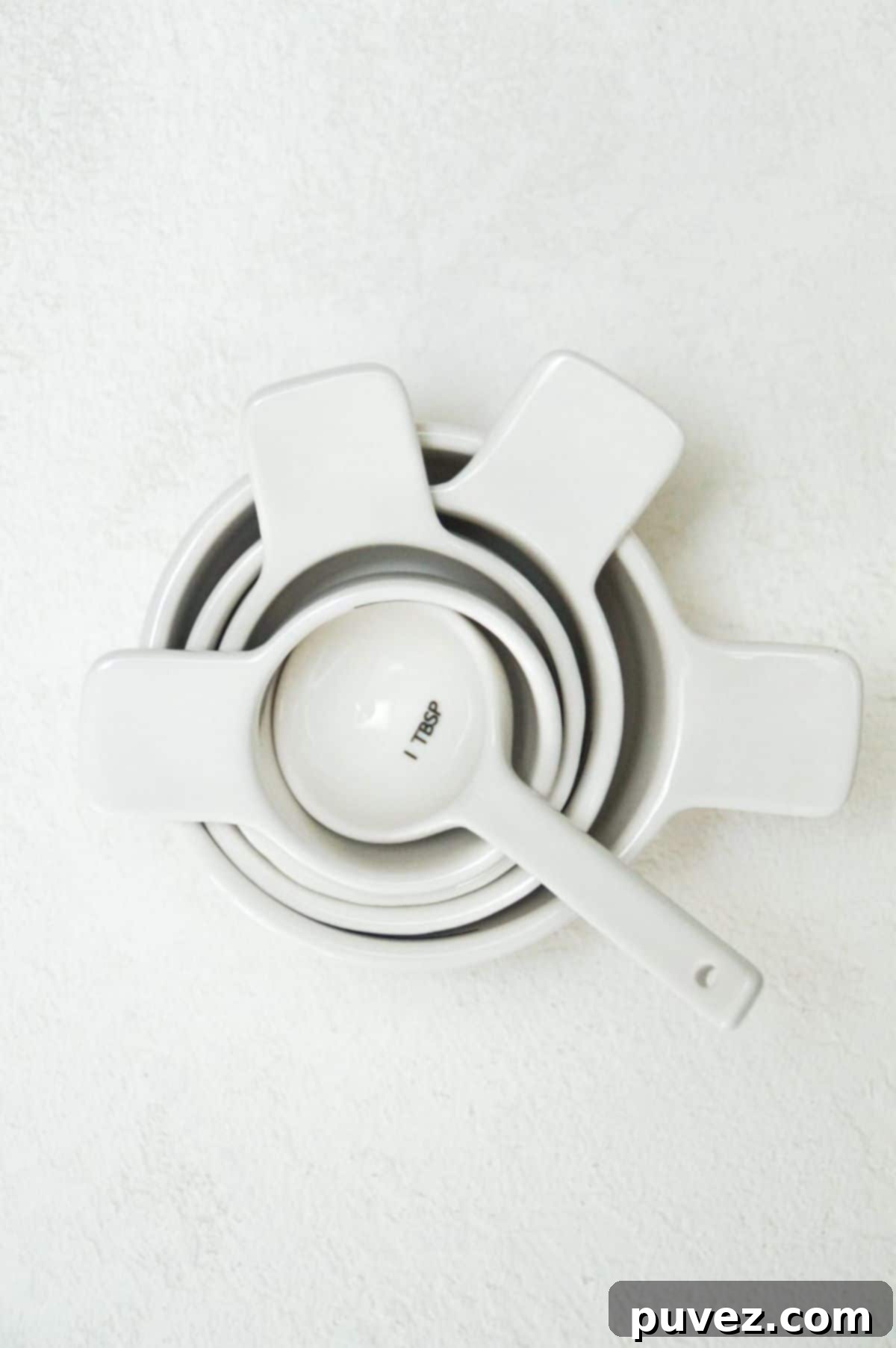 White measuring cups and one white tablespoon stacked, showcasing various measurement tools.