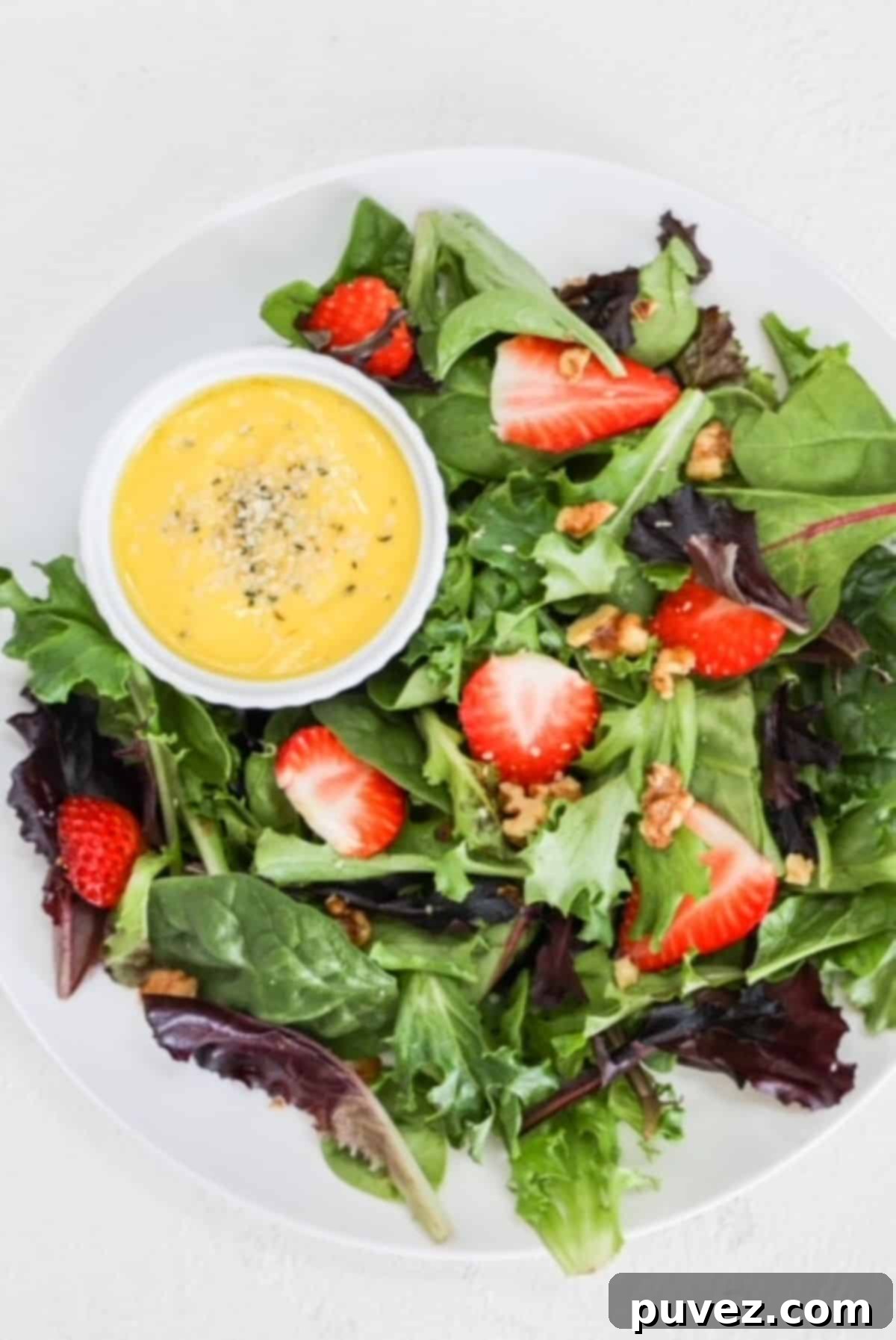 Effortless Mango Salad Dressing 2 A vibrant, creamy mango salad dressing drizzled over a fresh strawberry salad on a white plate, garnished with hemp hearts.