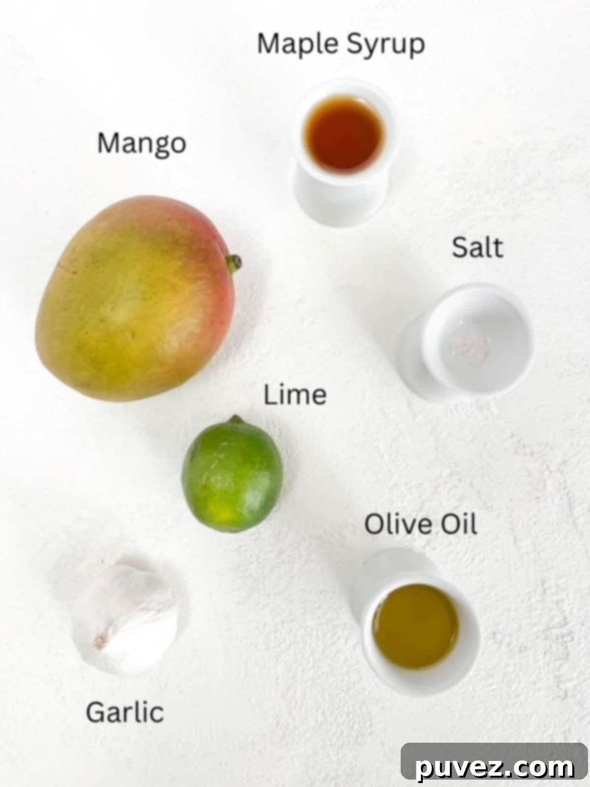 Effortless Mango Salad Dressing 3 Individual ingredients for mango salad dressing laid out, including a sliced mango, a lime, olive oil, maple syrup, and garlic.