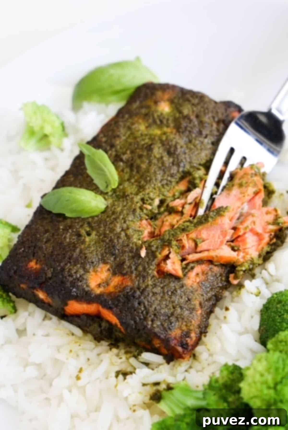 A fork cutting into a piece of cooked salmon topped with pesto.
