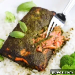A fork cutting into a piece of cooked salmon topped with basil pesto, served over rice.