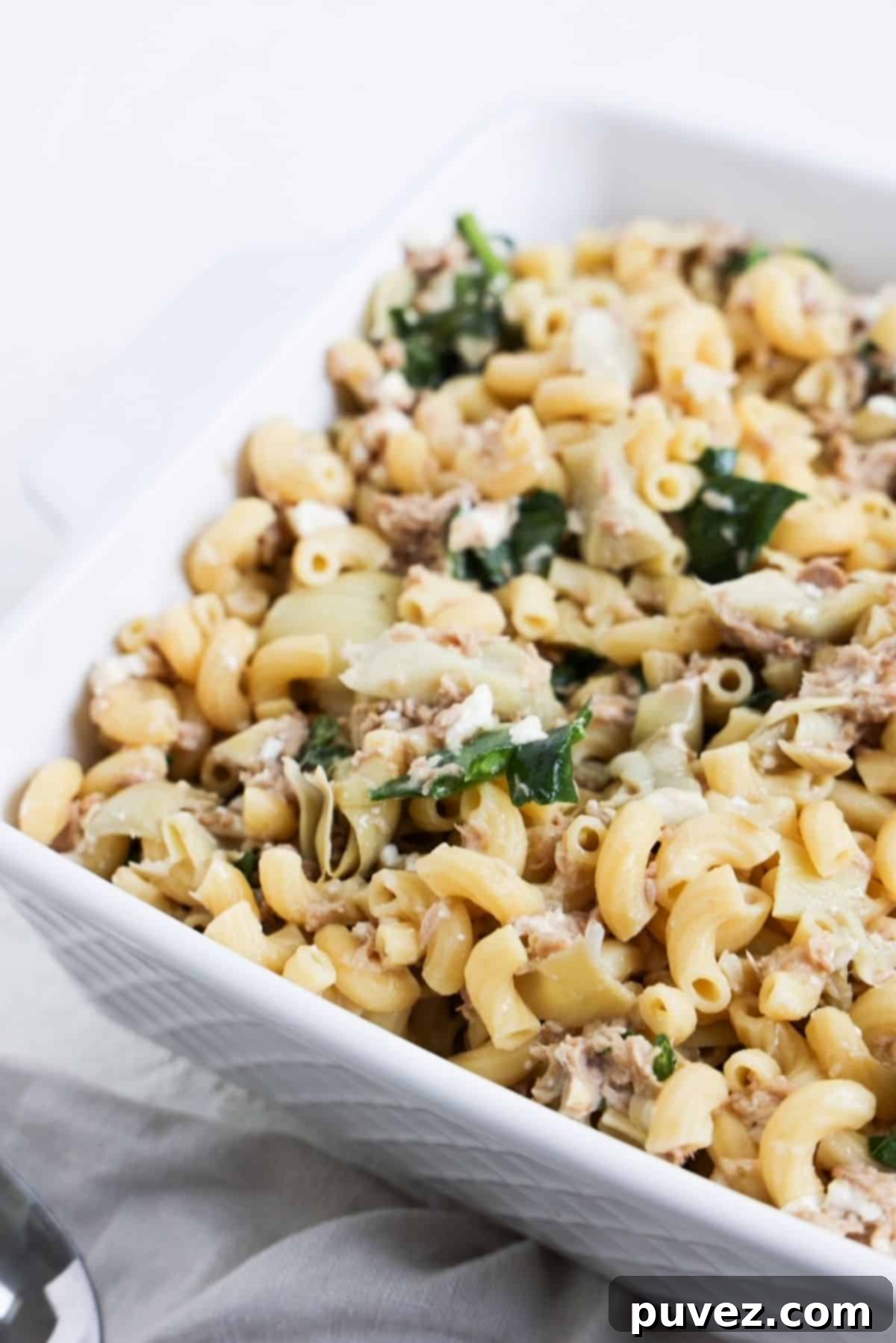 Partial view of this Tuna Pasta with Feta and Artichoke Hearts in a square white dish with a linen napkin to the left of the dish.