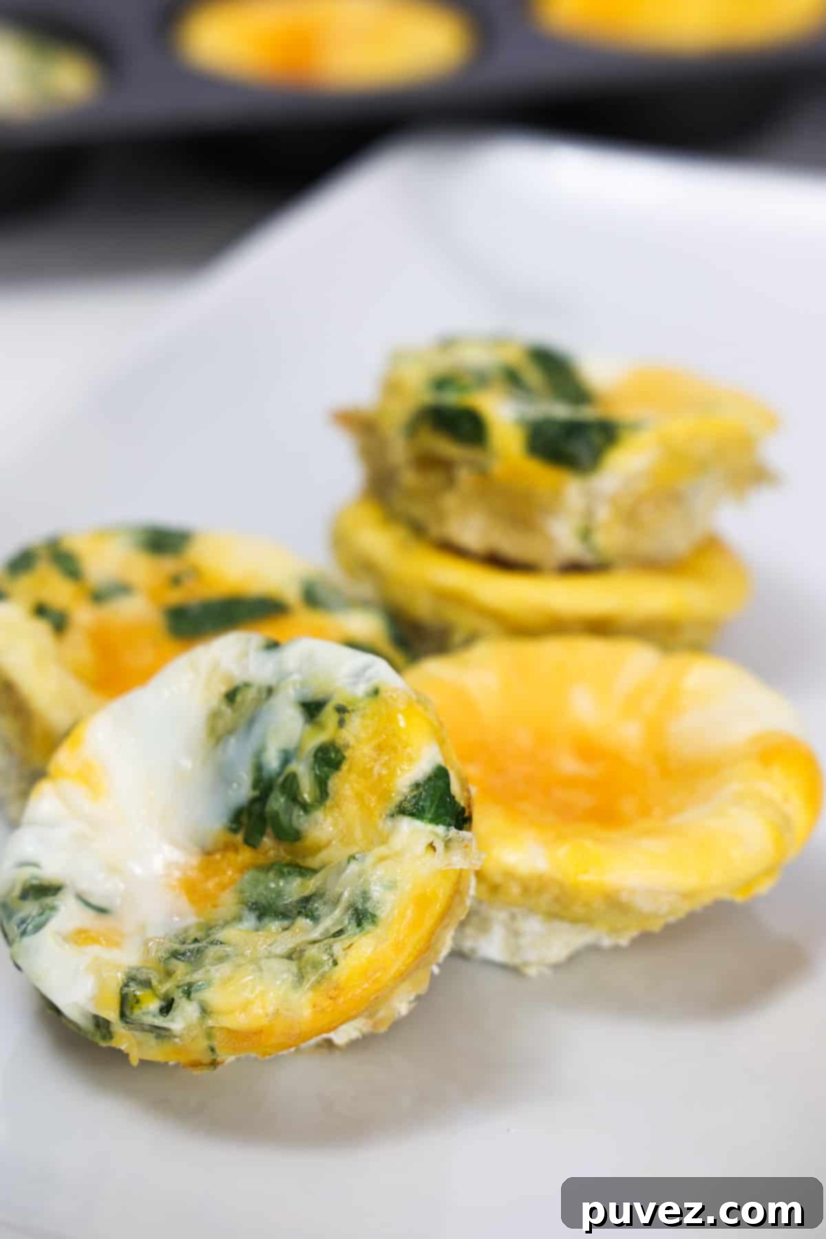 Baked egg muffins, some plain and some with spinach, on a white plate.
