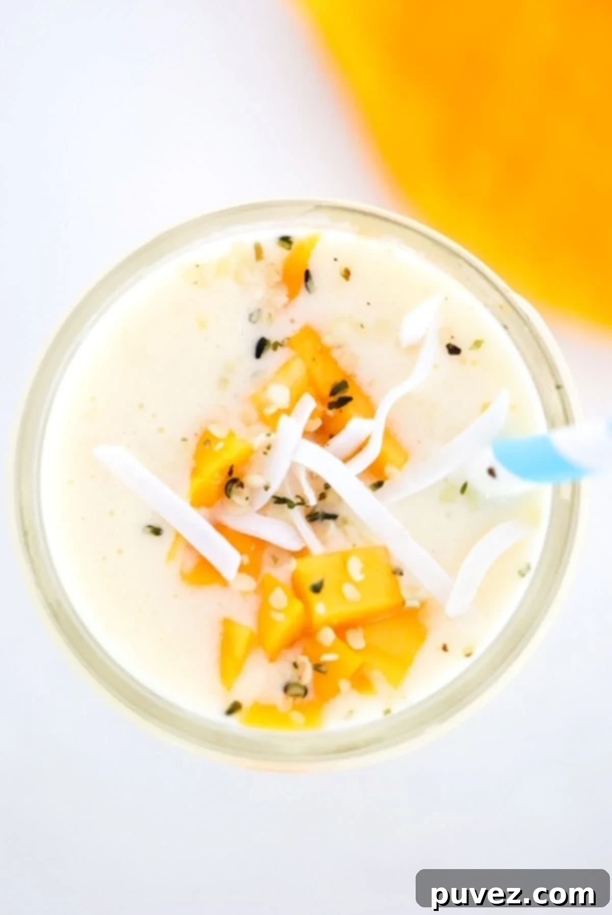 Creamy Mango Pineapple Smoothie topped with fresh mango pieces and delicate coconut flakes, served in a glass with a striped straw, inviting a taste of the tropics.