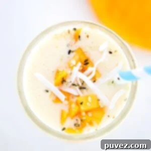 Creamy Mango Pineapple Smoothie topped with mango and coconut flakes with a blue and white striped straw, in a glass.