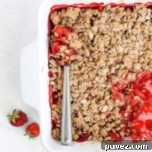 Effortless Strawberry Crumble 5 Top view of strawberry crumble in a white square baking dish with one serving of crumble removed and a serving spoon laid on top of the remainder of the crumble.