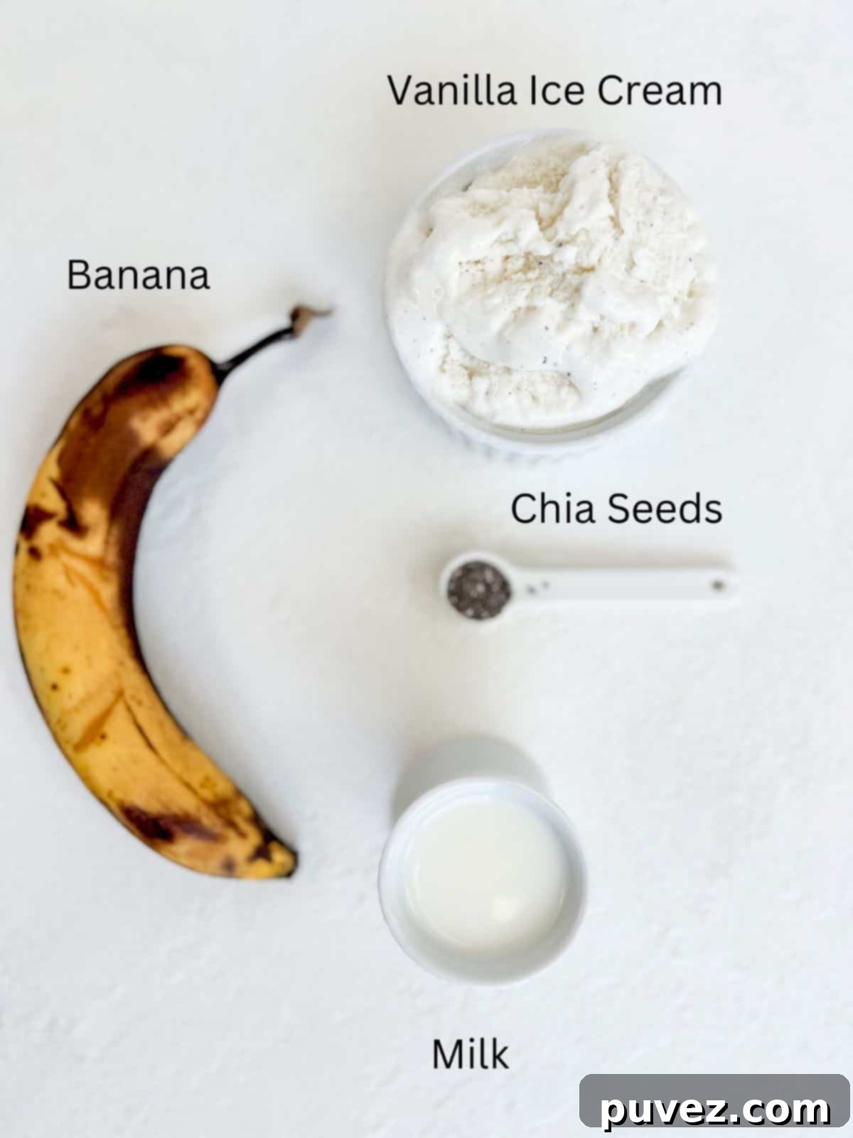 The four simple ingredients for the banana milkshake: a ripe banana, a scoop of vanilla ice cream, a small glass of milk, and a tiny spoon of chia seeds, all clearly labeled.