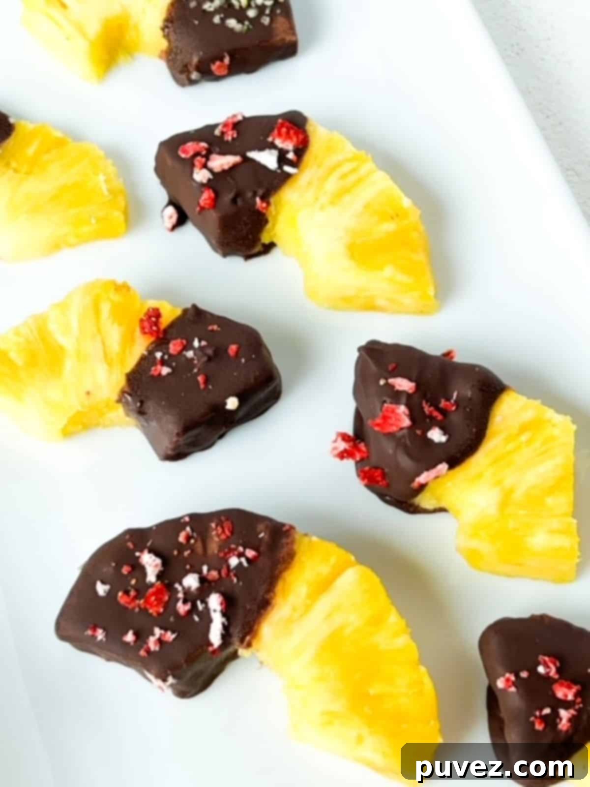 Thirds and halves of pineapple rings with one end covered in chocolate and topped with crushed freeze dried strawberries.