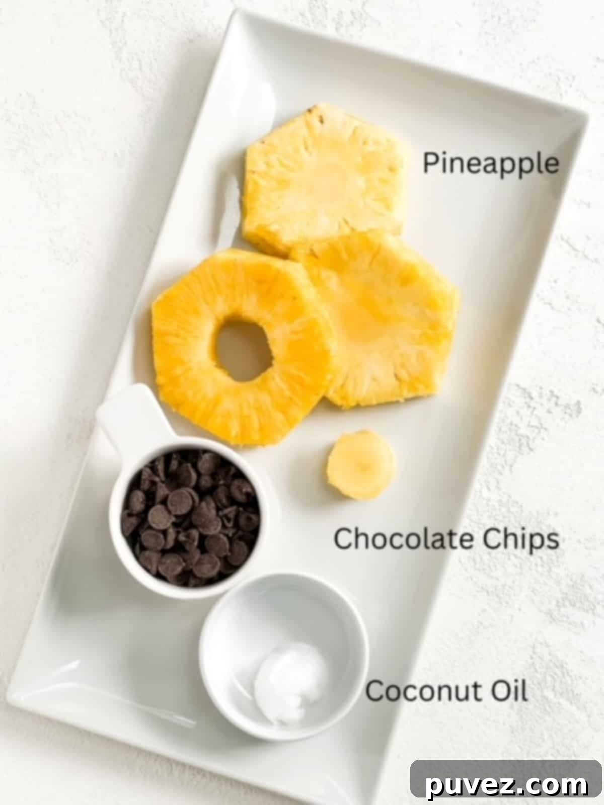 Pineapple rings, chocolate chips, and coconut oil labeled and on a white rectangular plate.