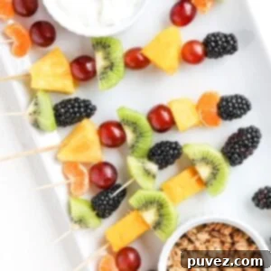 The Ultimate Fruit Skewers 4 A beautifully presented plate featuring an assortment of fresh fruit on toothpicks and bamboo skewers, accompanied by small ramekins of creamy yogurt and crunchy granola, perfect for a healthy and fun snack or party appetizer.
