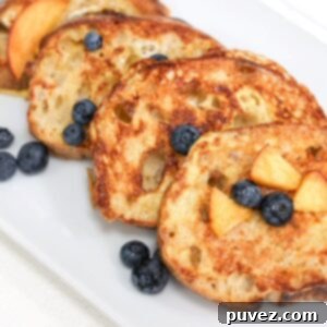 Four slices of golden sourdough French toast, artfully arranged and topped with juicy peach slices and fresh blueberries.