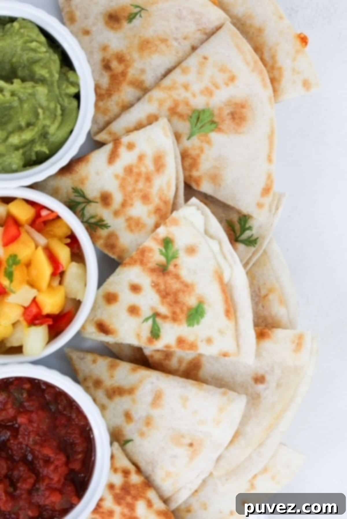 Pieces of cheese quesadillas plated with guacamole, mango pineapple salsa, and tomato salsa in separate white ramekins.