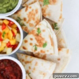 Pieces of a cheese quesadilla on a white plate with guacamole, mango salsa, and salsa.