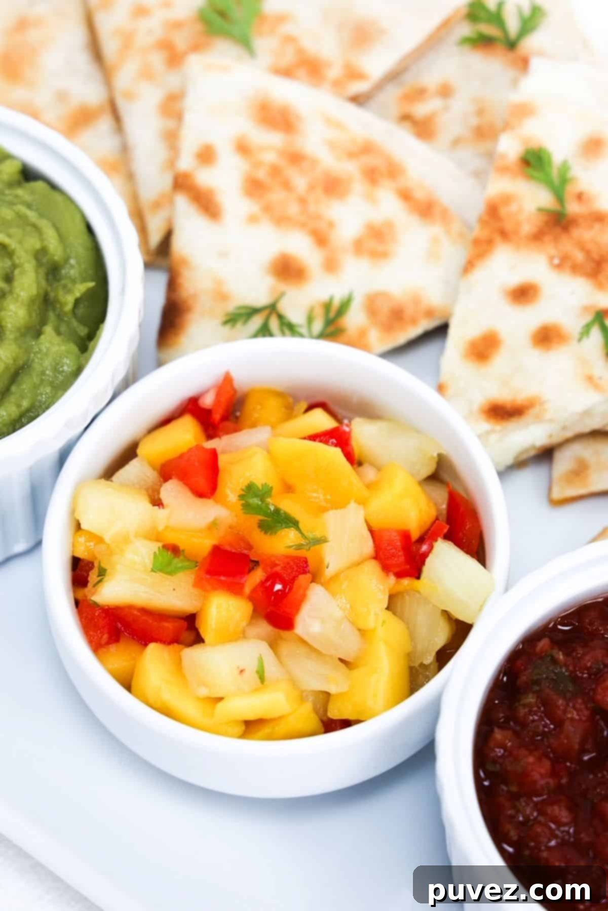 Pieces of cheese quesadilla plated with pineapple mango salsa, guacamole, and salsa.