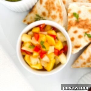 Pineapple mango salsa in a white ramekin with pieces of cheese quesadilla placed around it.