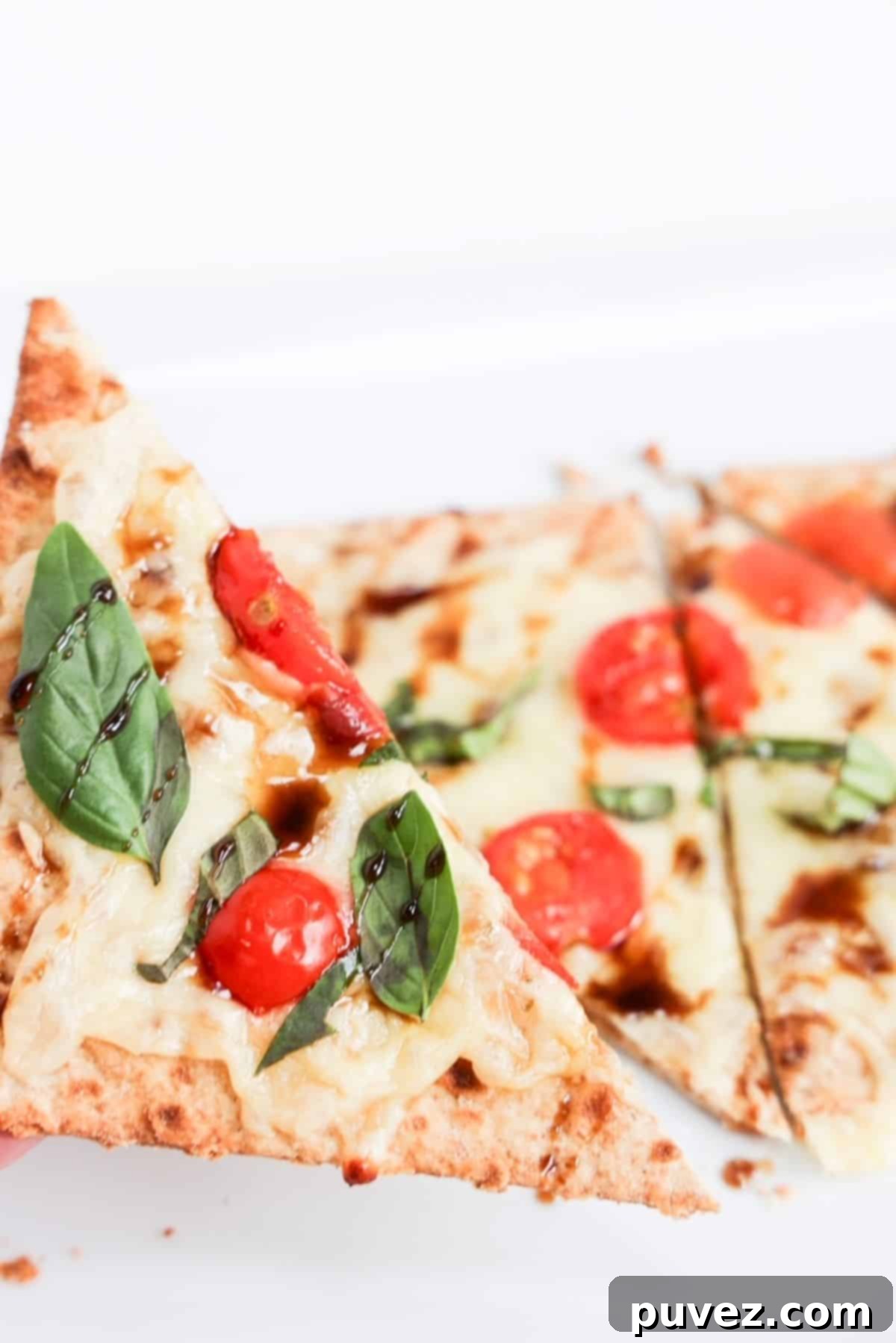 One piece of margherita flatbread held up close over the rest of the flatbread.