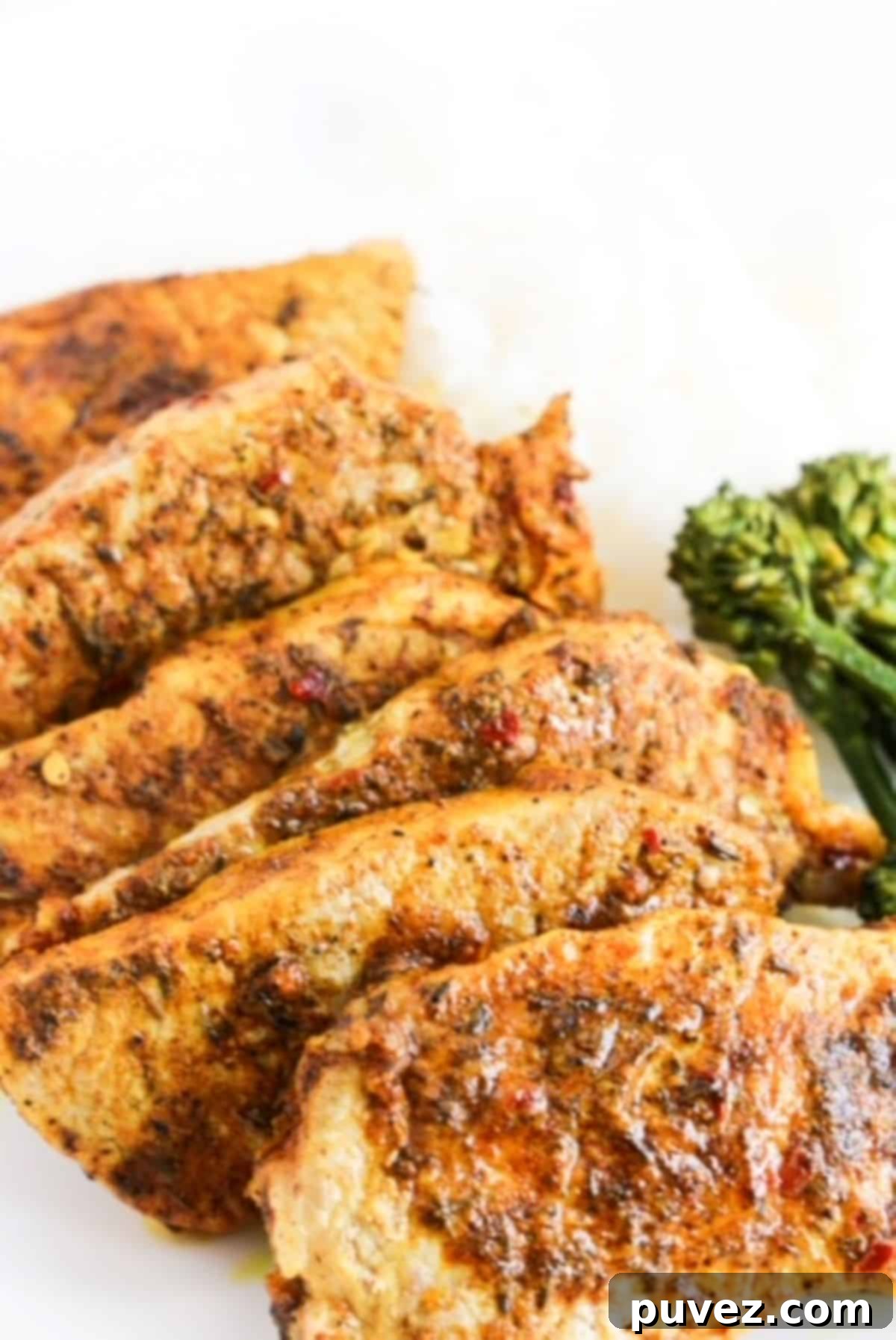 Six cooked jerk lime marinated pork chops overlapping each other on a white plate with broccolini to the right.