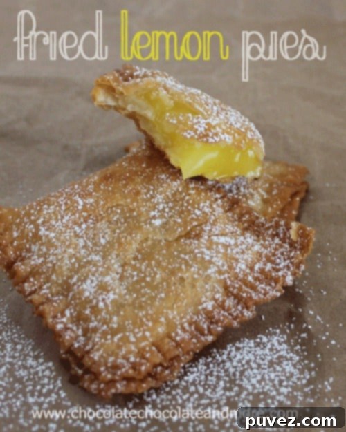 A close-up of a stack of golden fried lemon pies, dusted with powdered sugar.