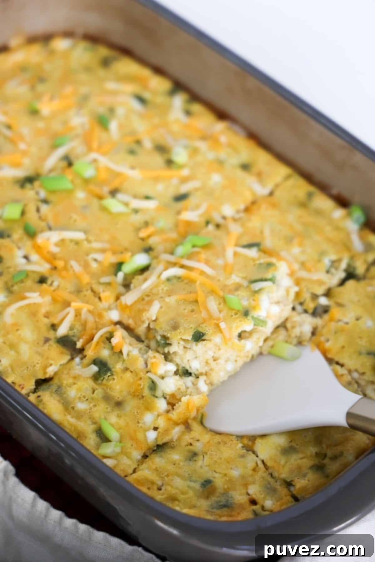 Green chile egg casserole in a large baking dish with one piece being removed with a white and gold spatula.
