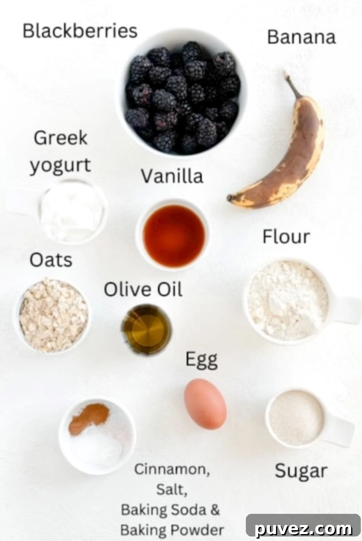 A vibrant flat lay of ingredients for Banana Blackberry Oatmeal Muffins, neatly arranged and labeled, showcasing fresh blackberries, ripe bananas, rolled oats, flour, Greek yogurt, egg, and olive oil.