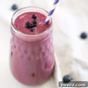 Blueberry Mango Tofu Smoothie with a purple and white striped straw. A linen napken with a few blueberries wraps around part of the base of the smoothie jar.