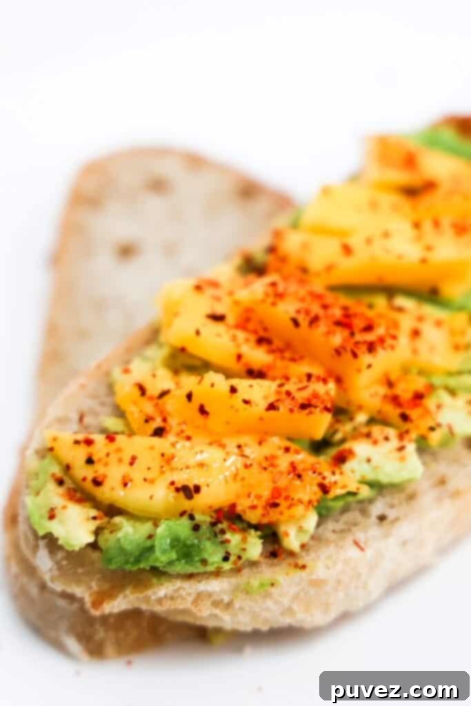 One piece of Mango Avocado Toast topped with Tajin on top of a plain slice of bread.
