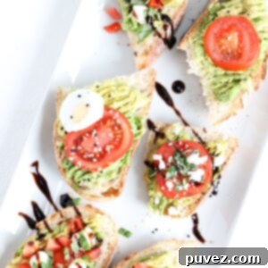 Six pieces of avocado toast topped with tomato and a variety of other topping that differ by piece. Served on a white platter.