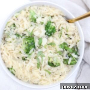 Quick and Creamy Broccoli Orzo 5 Top view of orzo with broccoli in a white serving dish with a gold serving spoon.