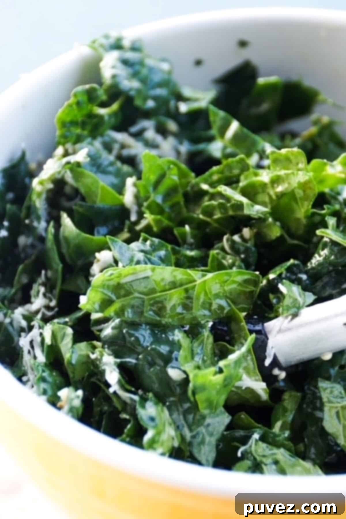 Kale salad in a yellow bowl with tongs.