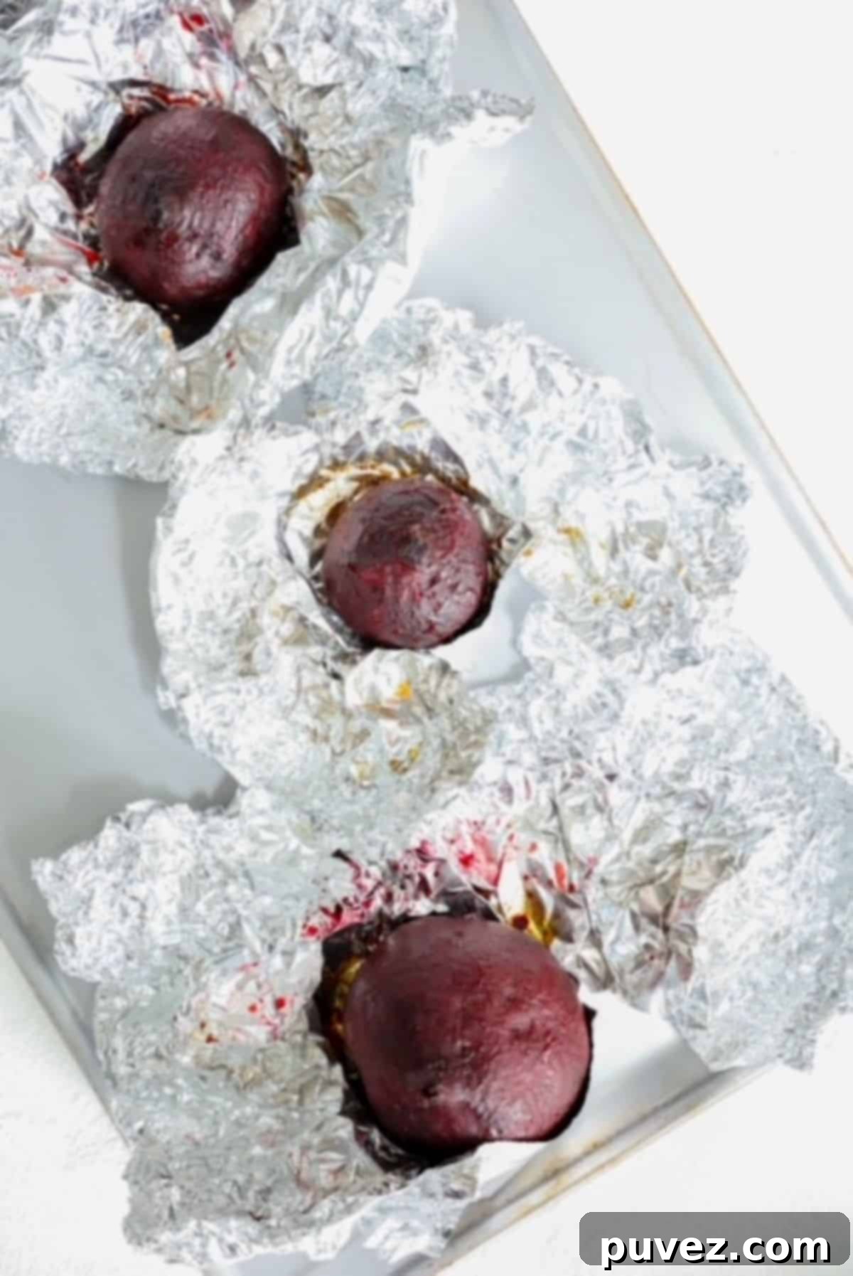 Three roasted beets on top of individual pieces of tinfoil. 