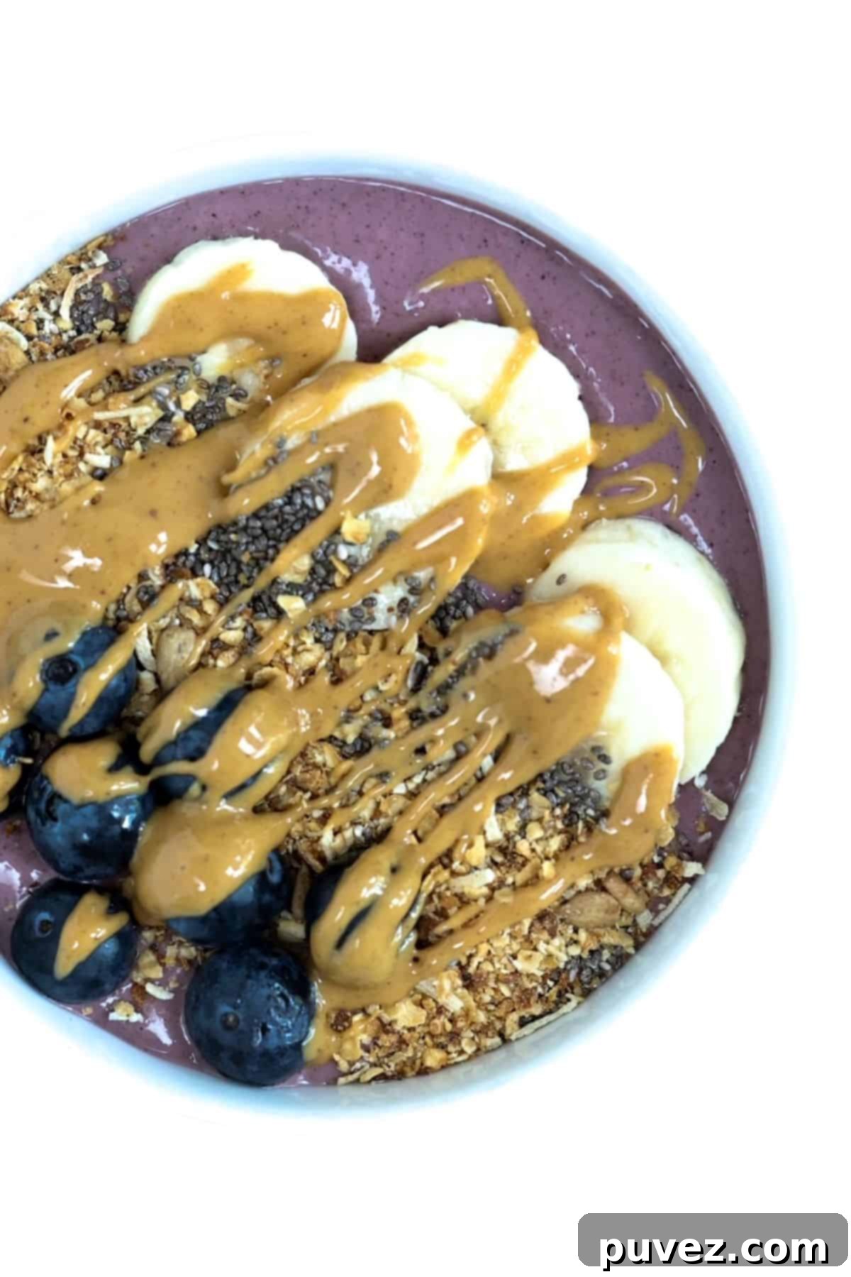 Top view of one acai bowl served in a white bowl, garnished with fresh fruit, granola, and chia seeds.
