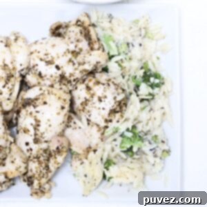 Pieces of baked Italian chicken thighs with a side of orzo and broccoli, presented on a plate.