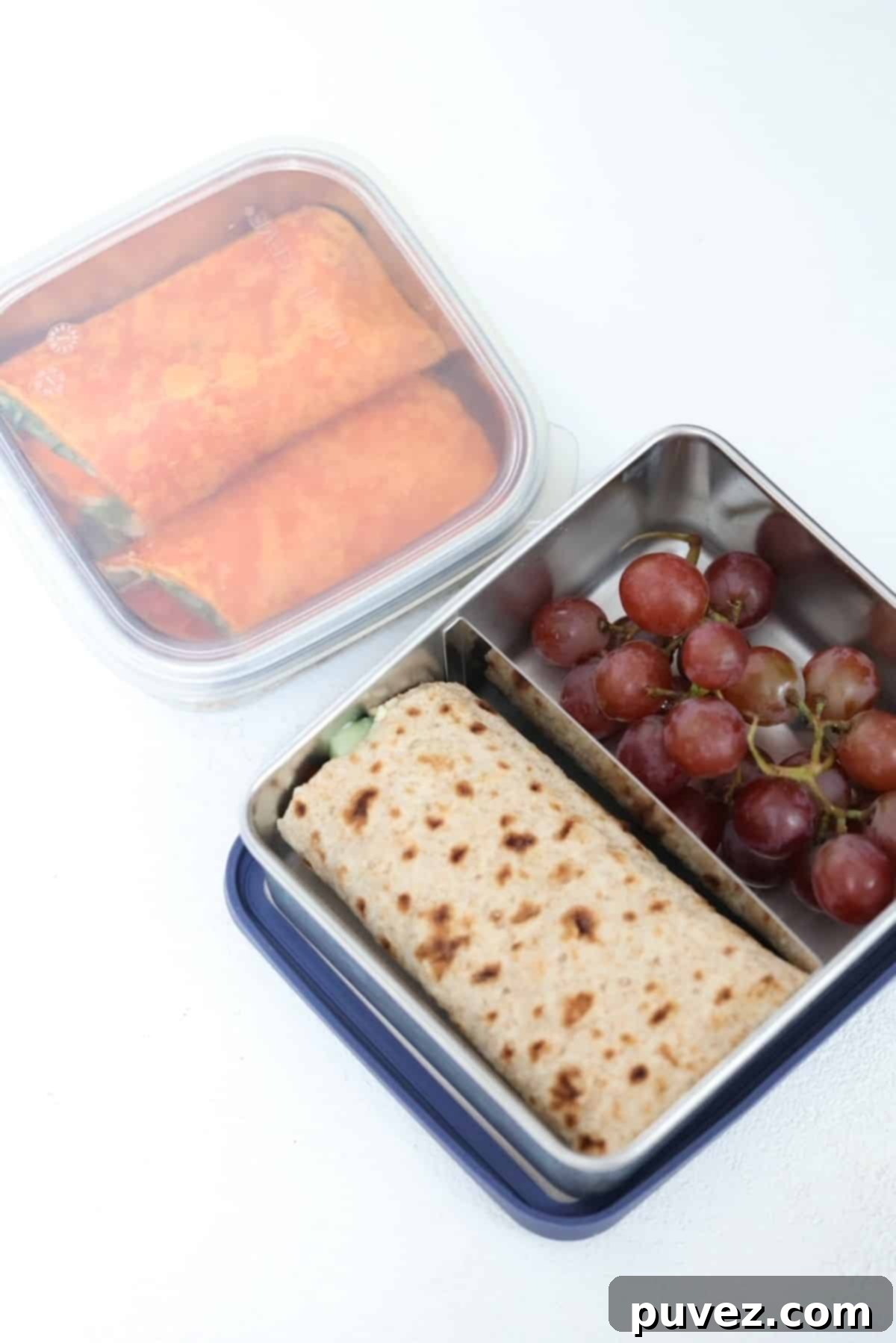 One lunch container with a wrap and the lid on and a double sided-lunch container with a wrap on one side and grapes on the other.