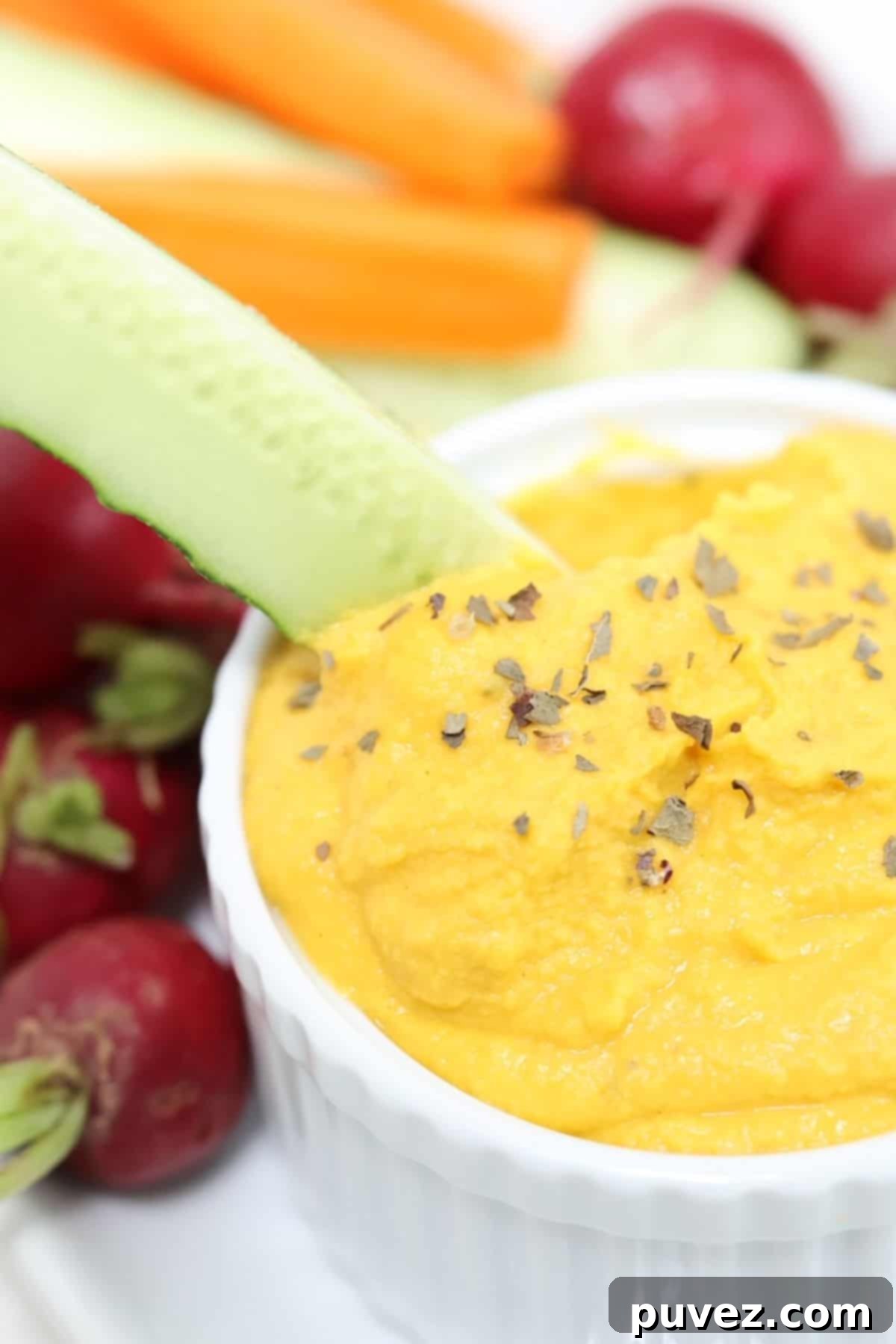 A cucumber spear being dipped into carrot hummus.