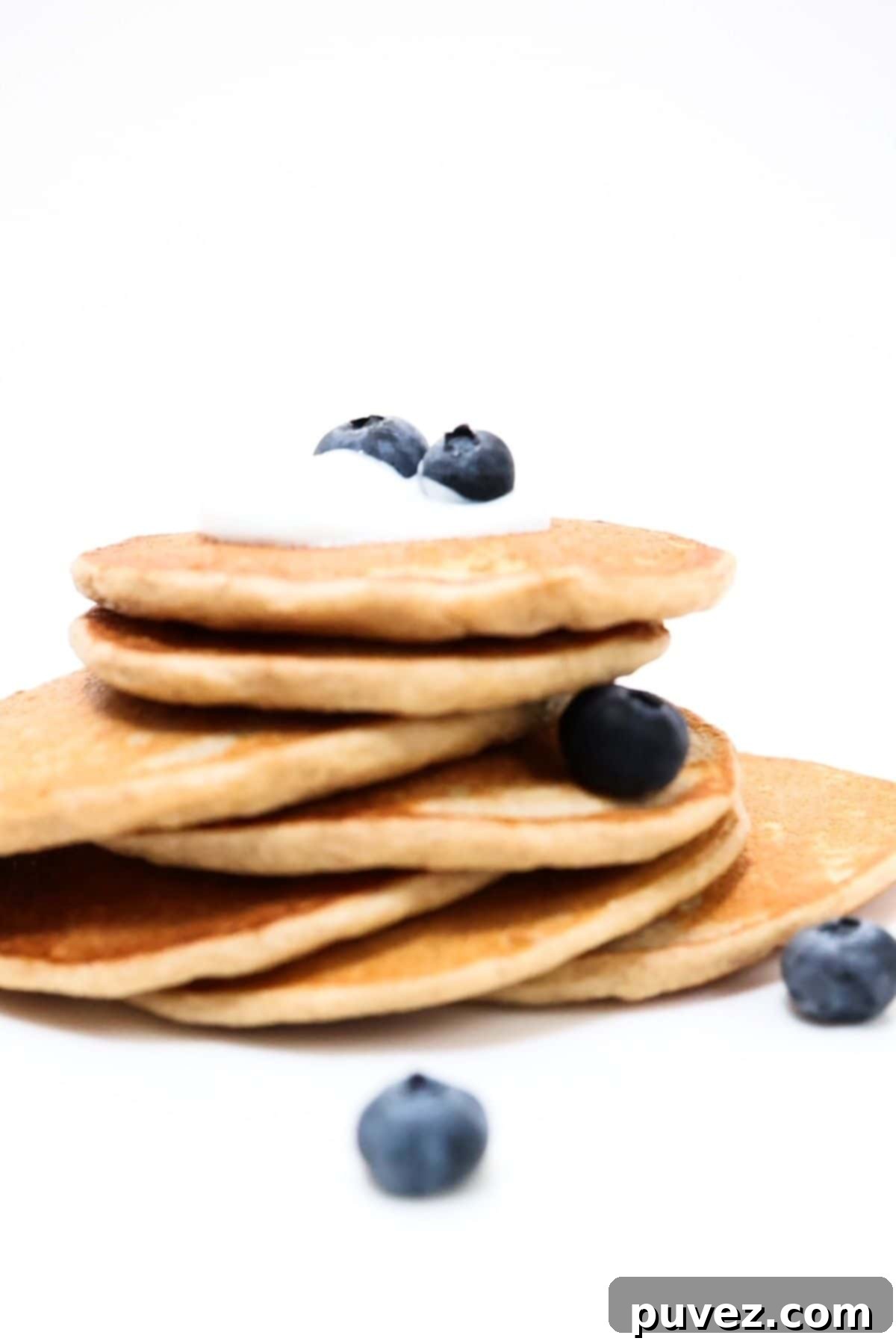 A stack of fluffy protein pancakes topped with a small amount of yogurt and fresh blueberries, ready for a healthy breakfast.