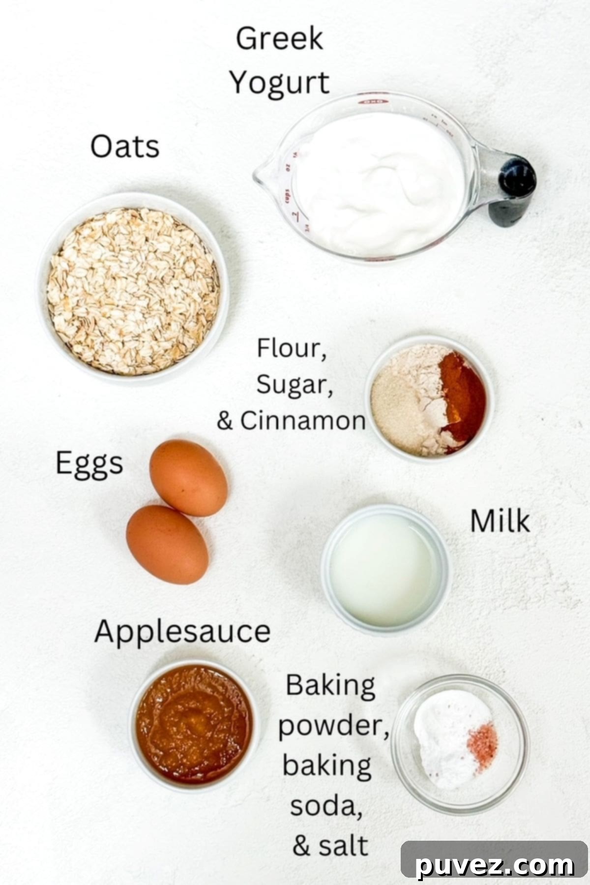 Protein pancake ingredients laid out on a table, including rolled oats, Greek yogurt, eggs, applesauce, flour, and spices, clearly labeled.
