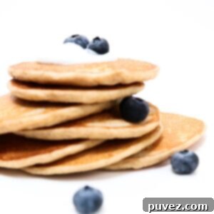 A stack of perfectly cooked protein pancakes, delicately topped with a small amount of creamy yogurt and a scattering of fresh blueberries.