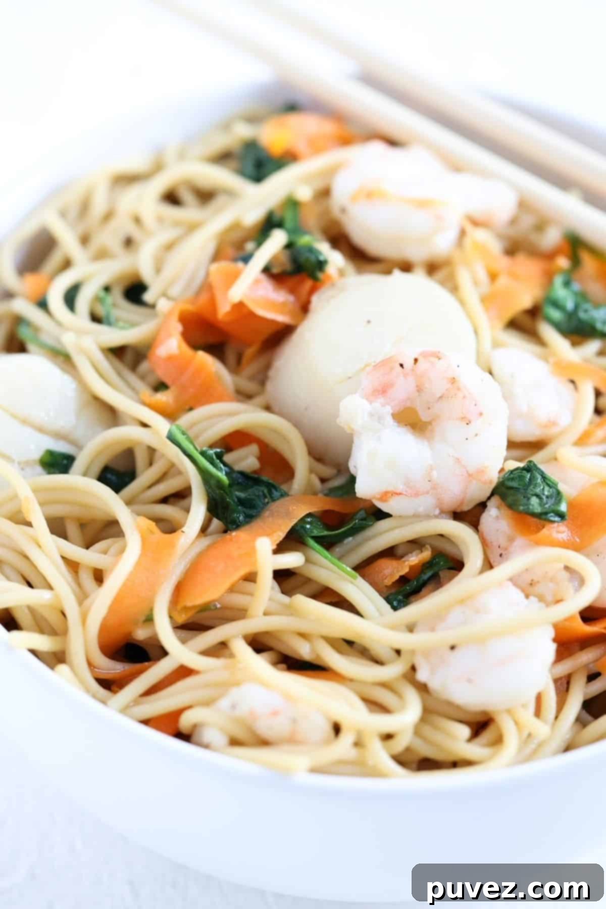 One noodle bowl with shrimp and scallops in a white bowl with chopsticks.