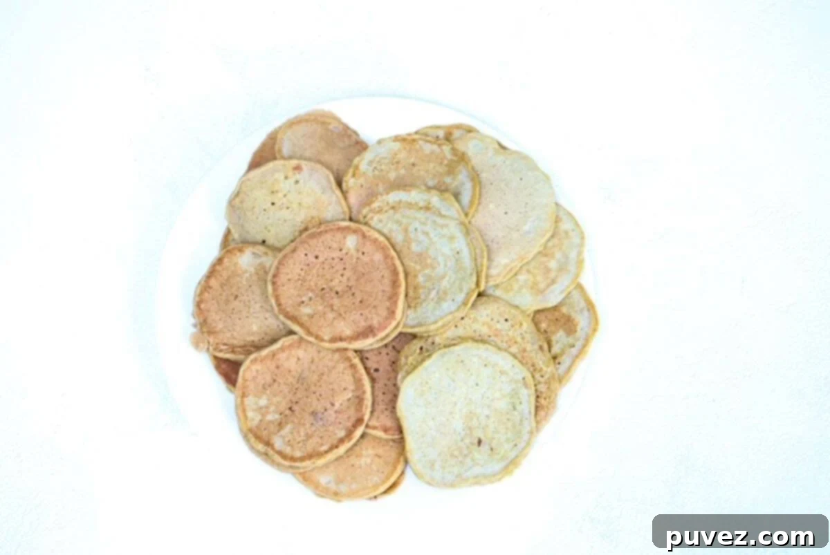 A white plate with a lot of pumpkin pancakes on it. Whole wheat pumpkin pancakes are to the left and pumpkin pancakes using pancake mix are to the right.