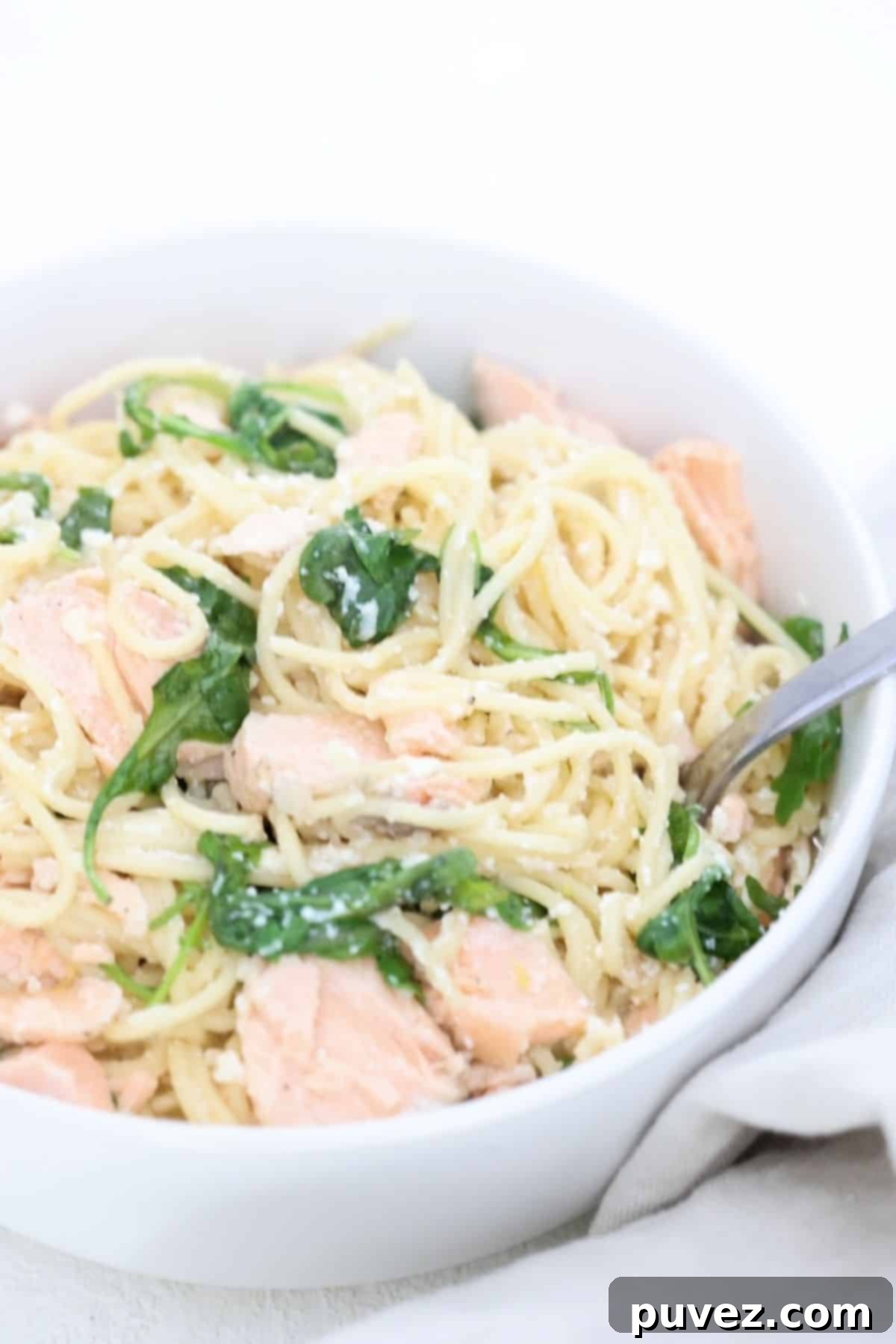 A creamy pasta dish with flaky salmon, fresh arugula, and lemon zest in a white bowl, with a fork ready to enjoy.