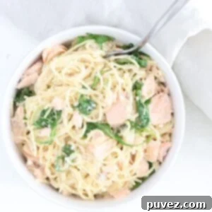 One bowl of creamy pasta with salmon and arugula in a white bowl with a fork.