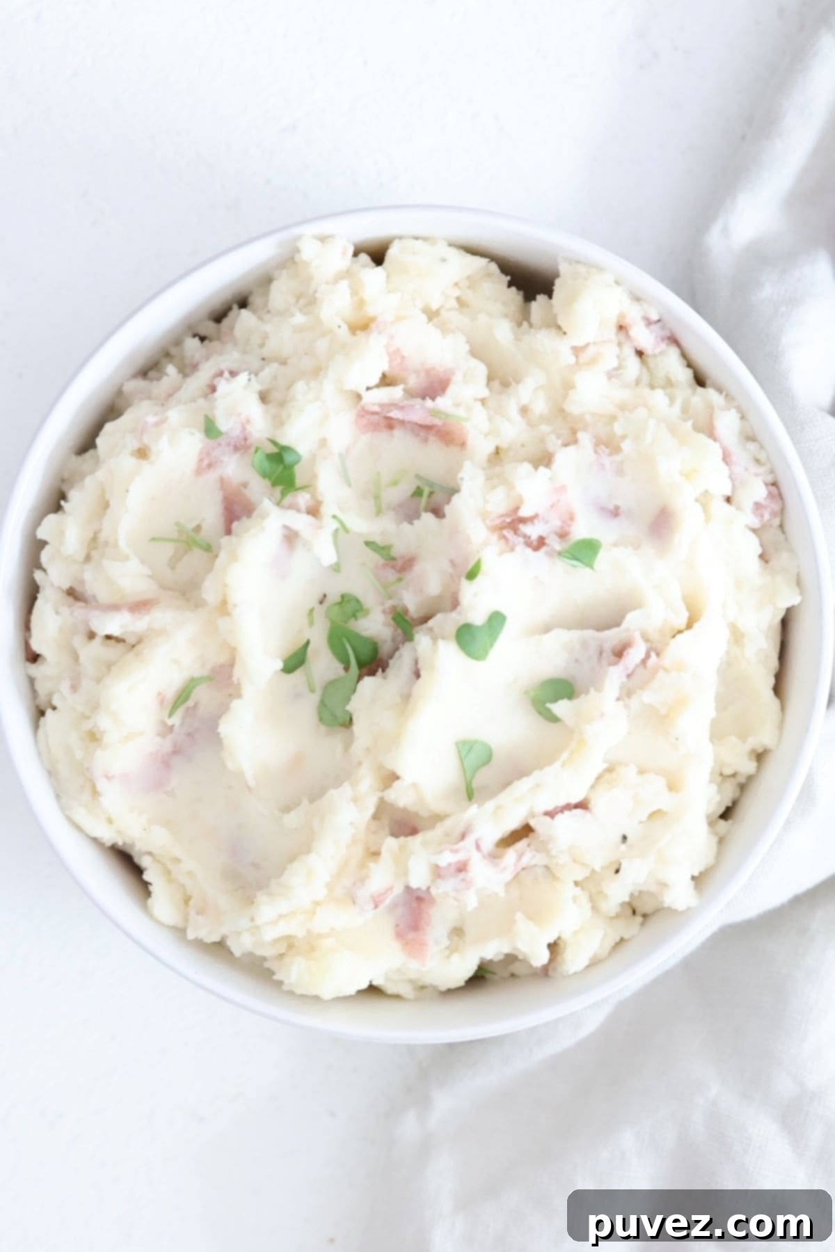 A white bowl filled with red skinned mashed potatoes topped with a few microgreens.