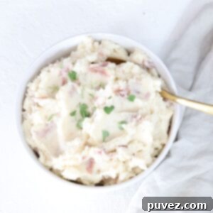 Easy Mashed Red Skinned Potatoes served in a white bowl with fresh green garnish.