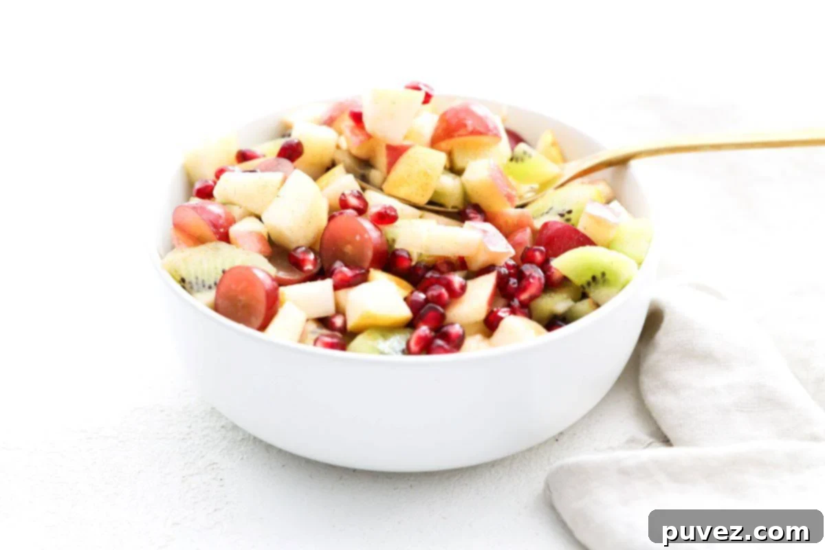 Autumn Fruit Medley 2 Fall fruit salad in a white serving bowl with a gold serving spoon.