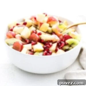 A vibrant holiday fruit salad in a white serving bowl with a gold serving spoon.