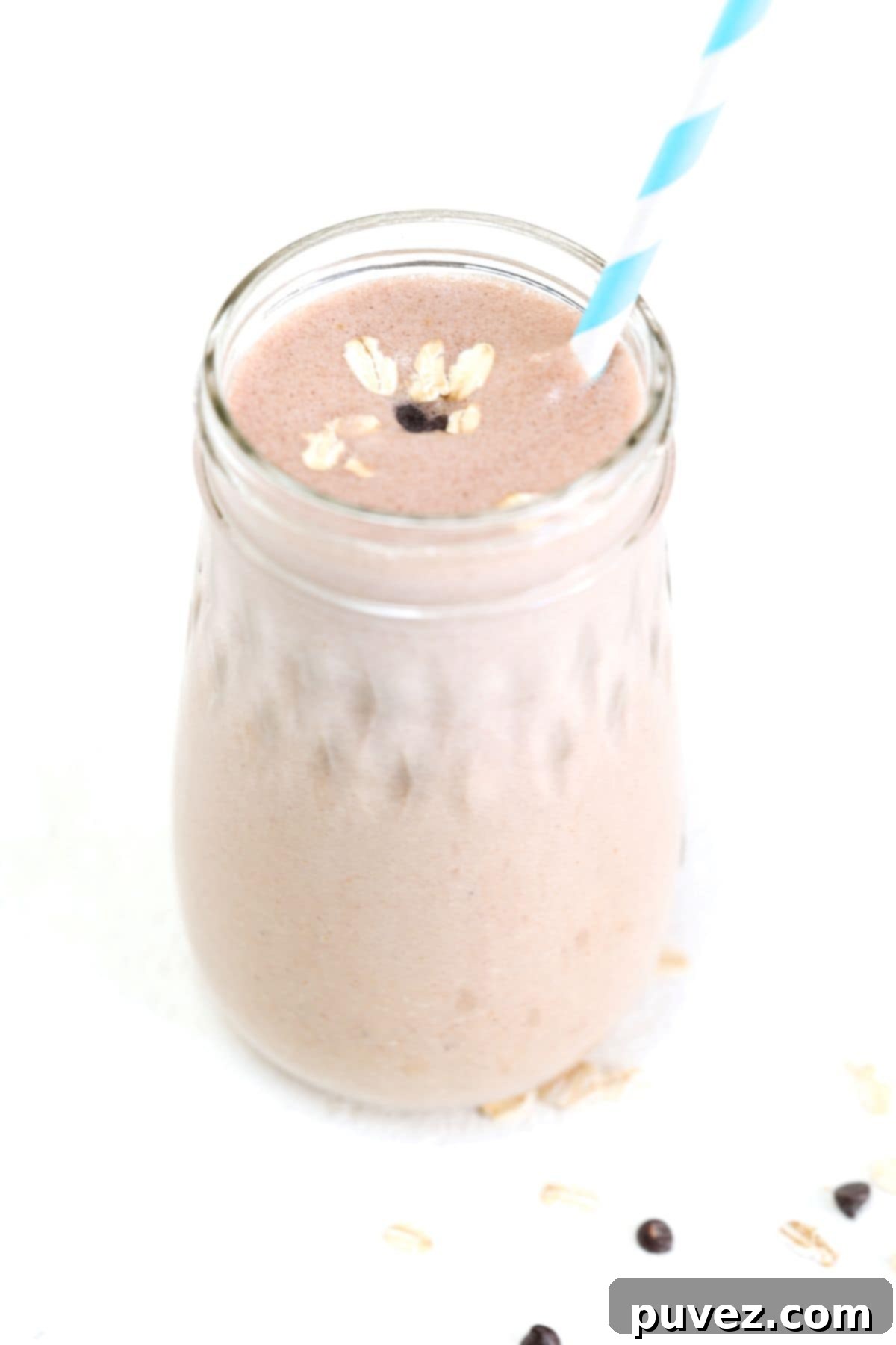 One peanut butter banana oatmeal smoothie in a glass jar with a blue and white striped straw.