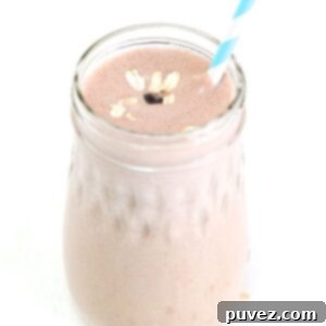 One Peanut Butter Banana Oatmeal Smoothie in a glass jar topped with oats and a mini chocolate chip, served with a straw.