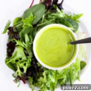 A crisp lettuce salad on a round white plate, accompanied by a small white bowl of vibrant green basil balsamic dressing, ready to be served.