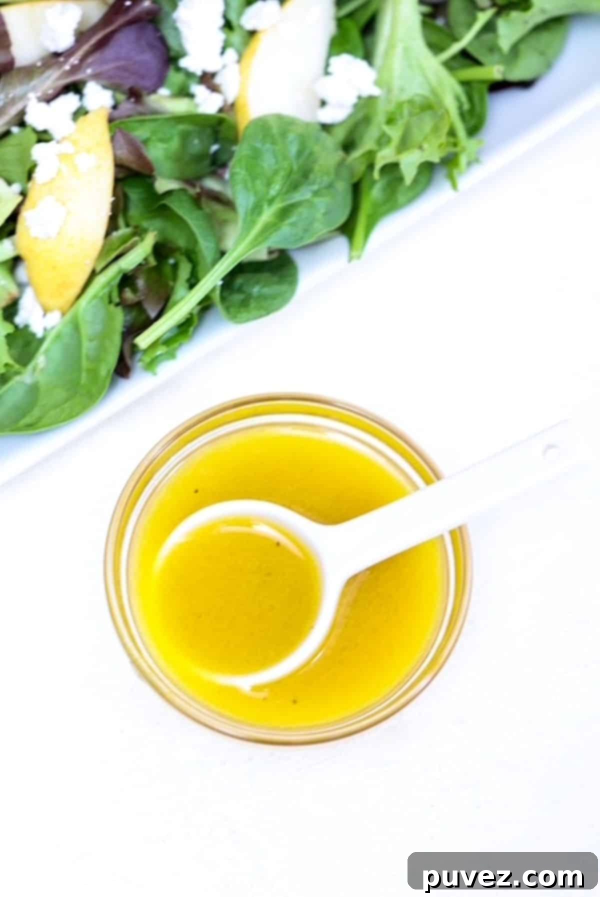 Bright Apple Vinaigrette 2 A small glass bowl filled with vibrant apple cider vinaigrette dressing, accompanied by a white spoon and a fresh green salad in the background, ready to be drizzled.