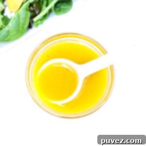 Bright Apple Vinaigrette 6 A small glass bowl filled with vibrant apple cider vinaigrette salad dressing, with a white serving spoon resting inside, ready for a fresh salad.
